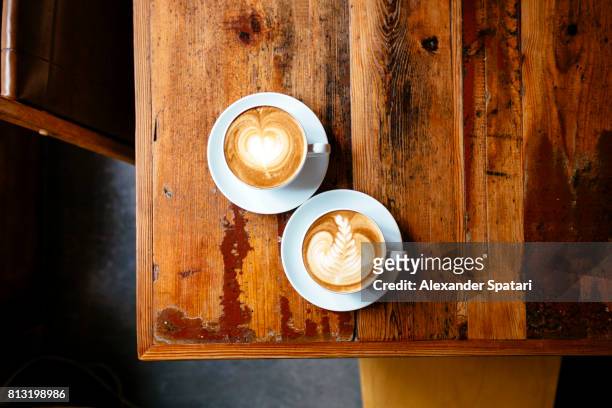 two cups of coffee with foam latte art on a wooden table seen from above - 2 cup of coffee stock pictures, royalty-free photos & images