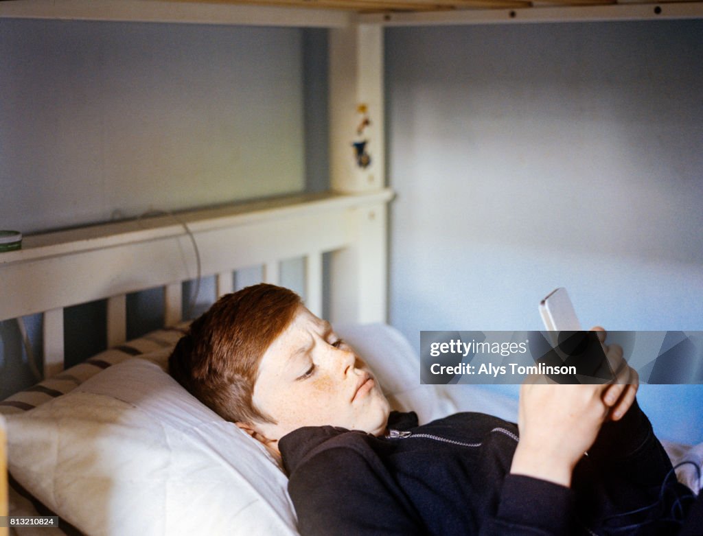 Teenage boy lying in bed looking at his mobile phone