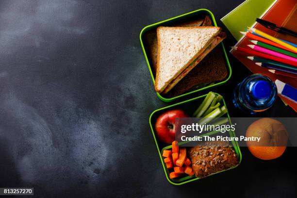 take out food lunch box with sandwiches and vegetables, bottle of water and school supplies copy space - slate pencil stock-fotos und bilder