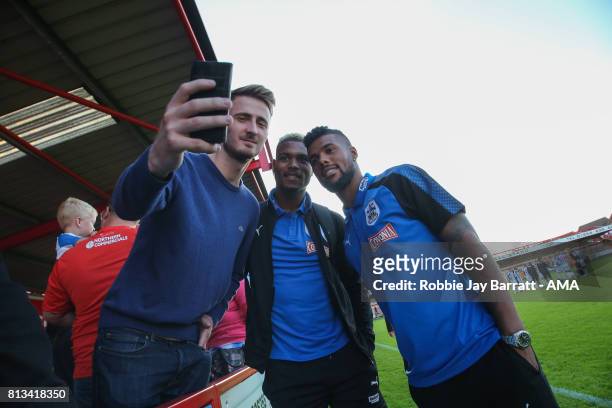 Steve Mounie of Huddersfield Town and Elias Kachunga of Huddersfield Town have a photo with a fan during the pre-season friendly match between...
