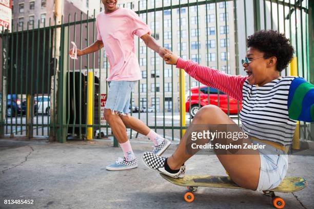 young man pulling a young woman on a skateboard - skating stock pictures, royalty-free photos & images