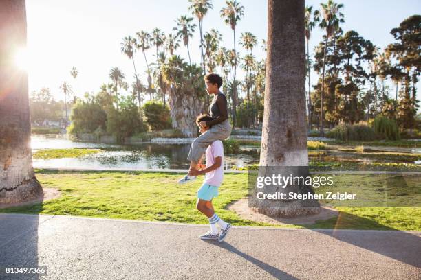 young man carrying his girlfriend on his shoulders - person auf den schultern tragen stock-fotos und bilder