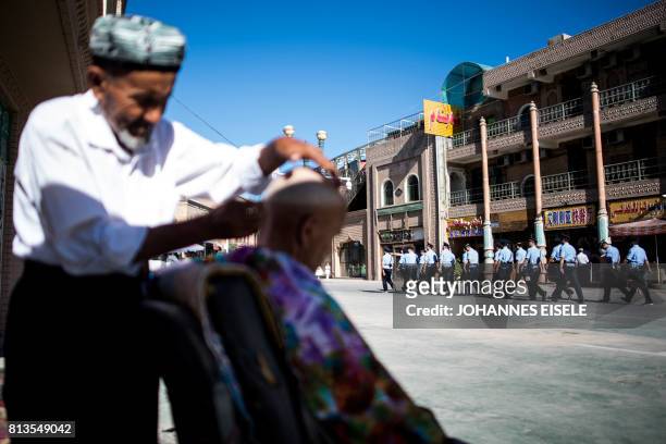This picture taken on June 26, 2017 shows police walking past a barber near the Id Kah Mosque in the old town of Kashgar in China's Xinjiang Uighur...