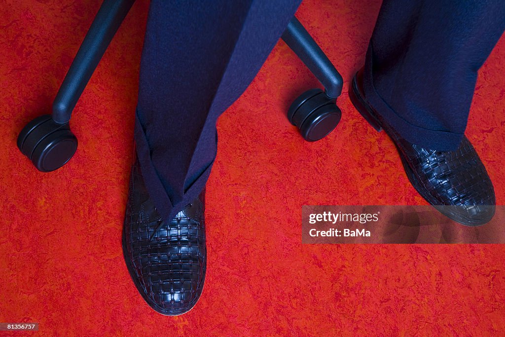 Black shoes of a businessman and office chair wheels on a red floor 