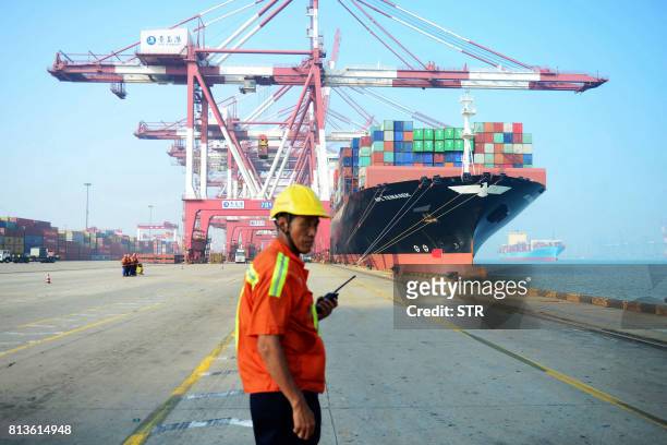 Chinese worker looks on as a cargo ship is loaded at a port in Qingdao, eastern China's Shandong province on July 13, 2017. China's exports rose a...