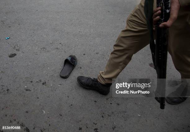 An Indian police officer walk past a lost slipper during funeral procession of a local rebel Sajad Gilkar, which was tear gassed Wednesday, July 12,...