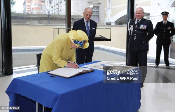 Queen Elizabeth II is watched by Prince Philip, Duke of Edinburgh and Deputy Commissioner of the Metropolitan Police Craig Mackey as she signs a book...