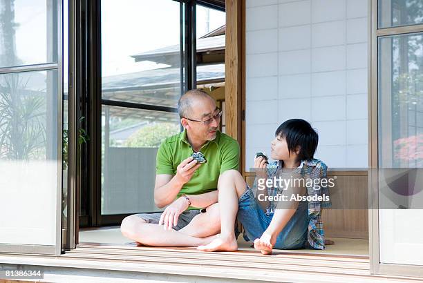 grandfather and grandson (8-9) sitting and eating rice ball in porch - rice ball stockfoto's en -beelden