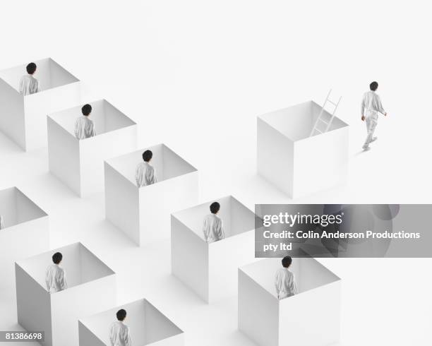 european businessman walking away from businessmen in boxes - stuck ストックフォトと画像