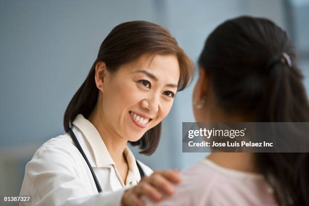 asian doctor reassuring hispanic female patient - korean female stock pictures, royalty-free photos & images