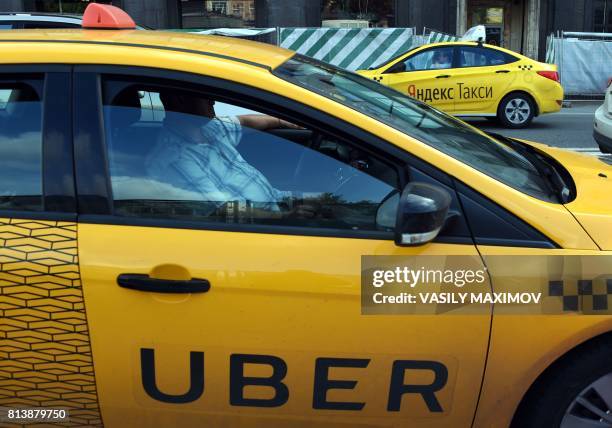 An Uber car and a Yandex.Taxi car drive on a street in Moscow on July 13, 2017. Uber on July 13, 2017 announced that it was merging in Russia and...
