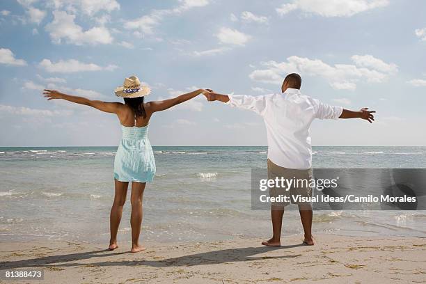 african couple with arms outstretched at beach - barefoot men stock-fotos und bilder