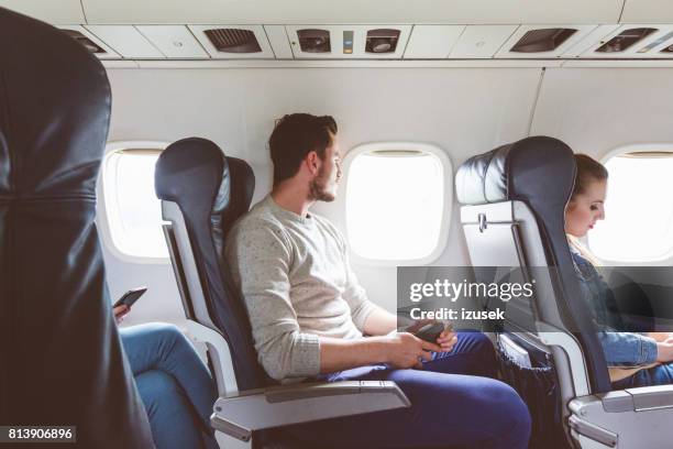 young man sitting in airplane near window - plane passenger stock pictures, royalty-free photos & images