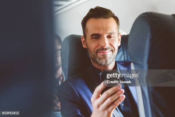 man travelling by plane and using mobile phone - business class imagens e fotografias de stock