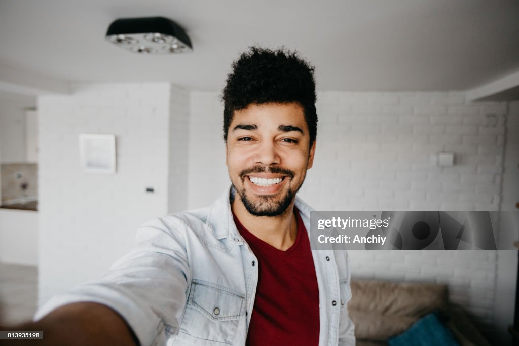 Lächelnd Mann im Wohnzimmer ist eine Selfie nehmen.
