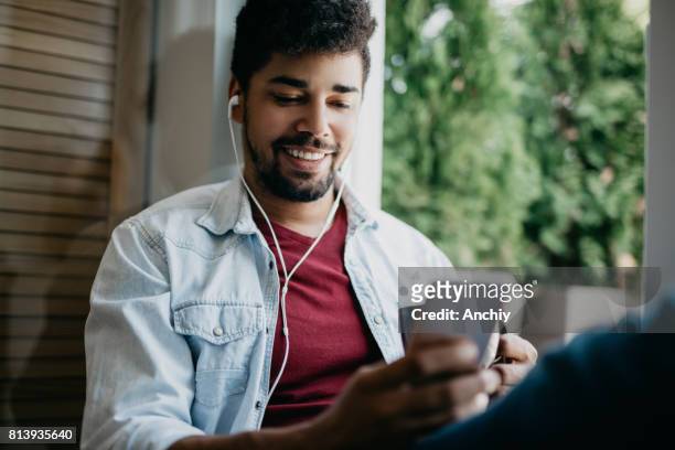 lächelnd mischlinge mann nutzt handy, um musik zu hören - listening stock-fotos und bilder