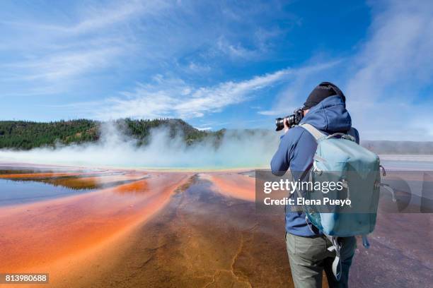 photographer on grand prismatic spring with puffy clouds overhead in yellowstone national park, wyoming. - yellowstone photos et images de collection