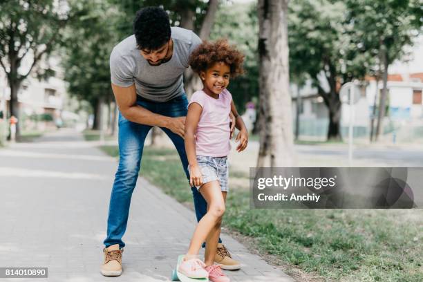 smiling preschool girl with her dad at the park skateboarding - father longboard stock pictures, royalty-free photos & images