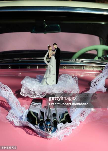Vintage bride and groom wedding cake topper adorns the hood of a pink 1955 Cadillac Series 62 at a Fourth of July classic car show in Santa Fe, New...