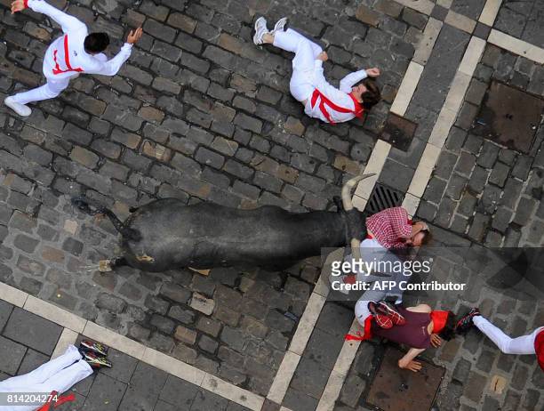 Participants fall past a Miura's fighting bull during the eighth and last bull run of the San Fermin festival in Pamplona, northern Spain on July 14,...