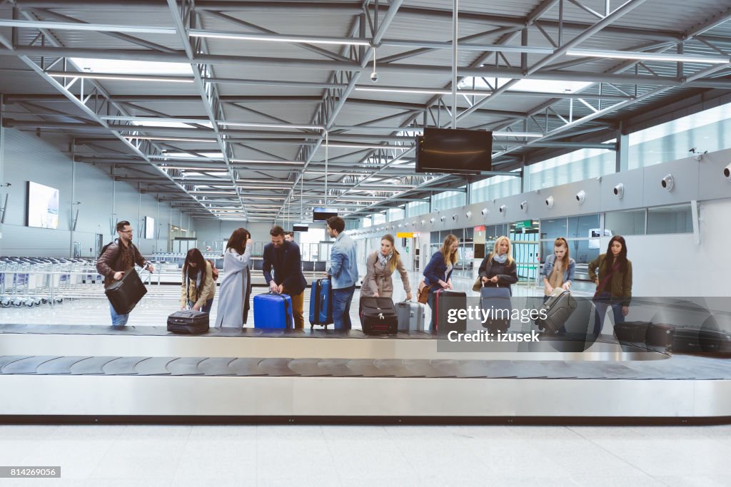 Passengers collecting baggage from luggage conveyor belt at airport