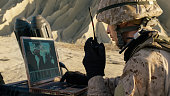 Soldier is Using Laptop Computer and Radio for Communication During Military Operation in the Desert.