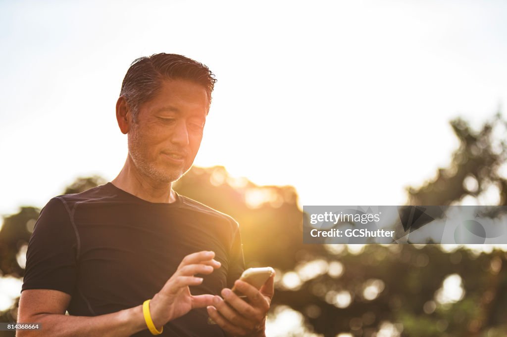Mature Japanese man using his smart phone early in the morning during his walk
