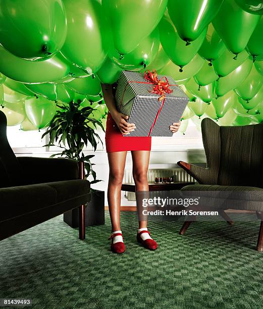 girl holding a present in a room filled with baloons - excess photos et images de collection