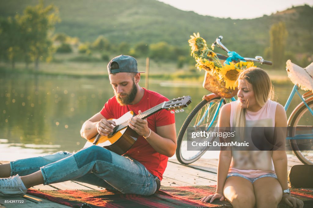 Couple playing guitar in sunset pier happy together