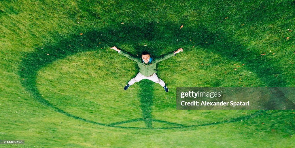 Happy smiling man laying on the peace symbol on the grass