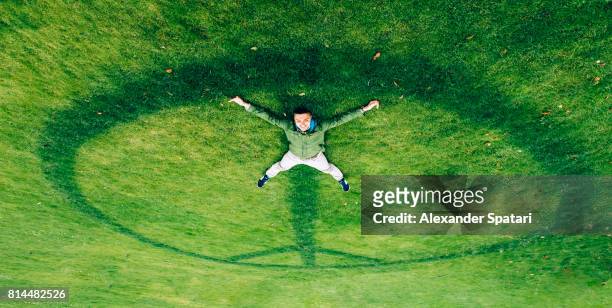 happy smiling man laying on the peace symbol on the grass - human limb stock pictures, royalty-free photos & images