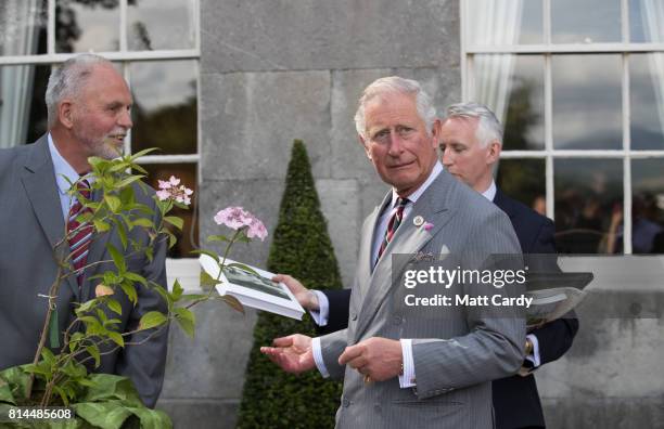 Prince Charles, Prince of Wales receives a gift from Anthony Tavernor owner and restorer of the Plas Cadnant Hidden Gardens as he vists the gardens...