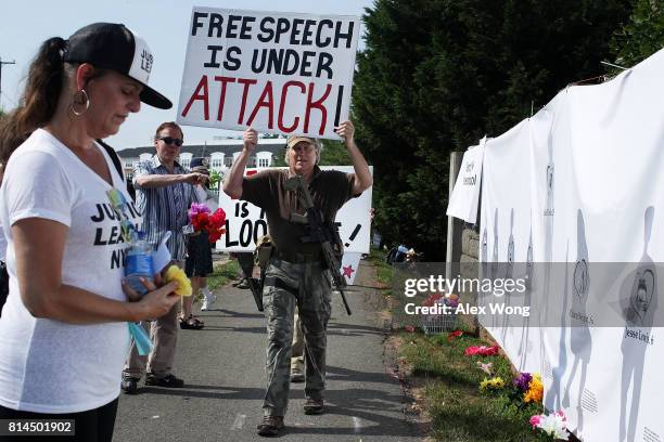 An armed gun rights activist counter-protests as he passes by a woman who pauses for a moment in front of the art piece "Reflections of Ourselves," a...