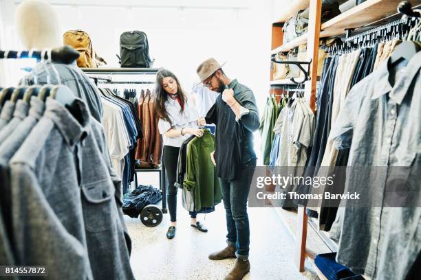 shopkeeper helping man decide on shirts while shopping in mens clothing boutique - kläder bildbanksfoton och bilder