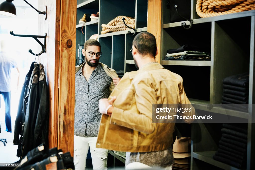 Man trying on jacket while looking in the mirror in mens clothing shop