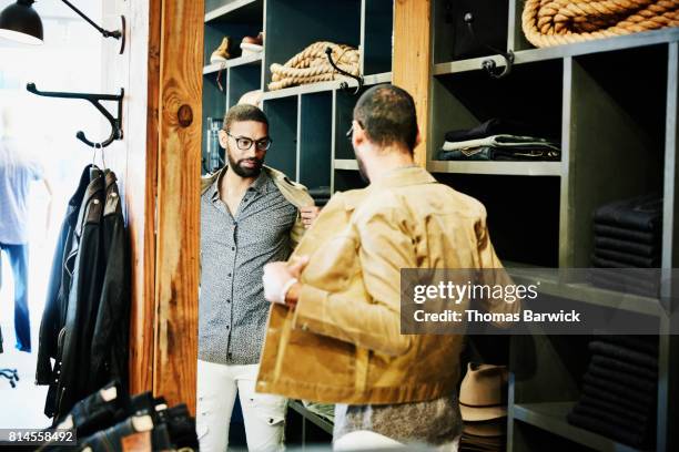 man trying on jacket while looking in the mirror in mens clothing shop - dressing room fotografías e imágenes de stock