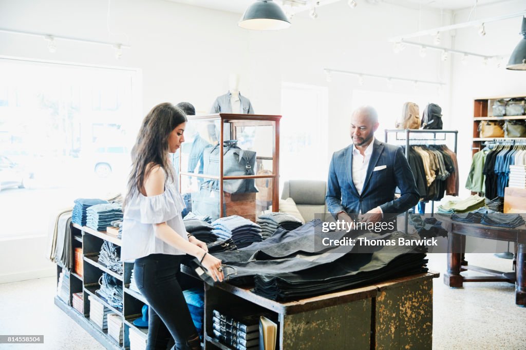Shopkeeper helping customer choose from a selection of denim in mens clothing boutique