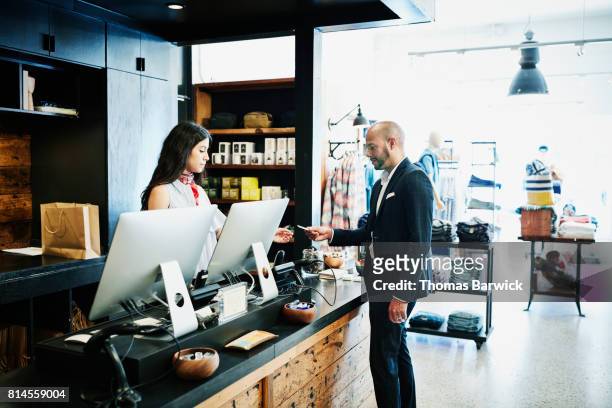man handing shopkeeper credit card after shopping in mens boutique - boutique shopping stock pictures, royalty-free photos & images