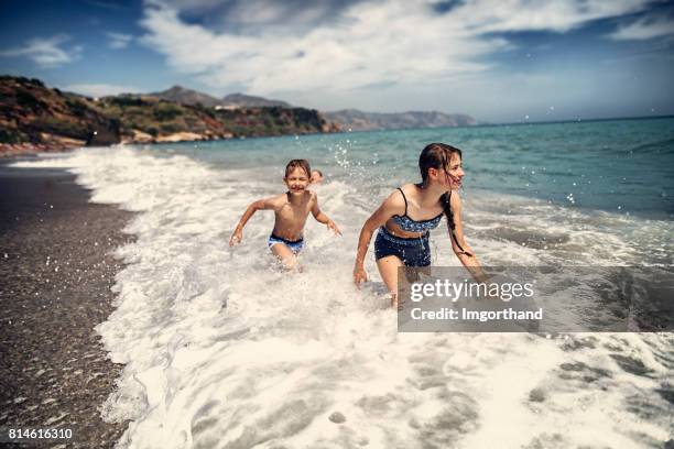 children enjoying waves on costa del sol beach, nerja, spain - nerja stock pictures, royalty-free photos & images