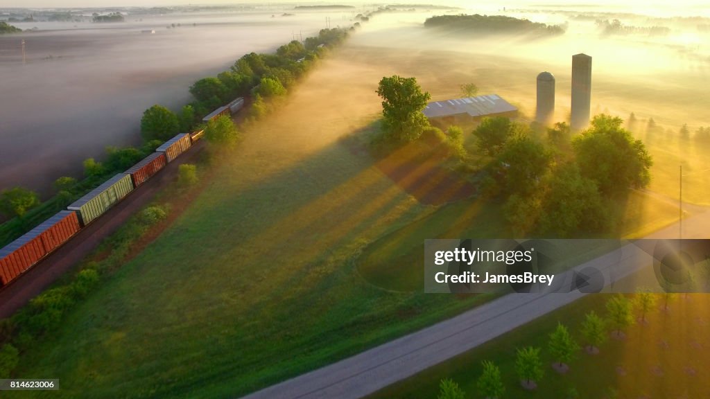 Trein rolt over mistige rurale landschap bij dageraad.