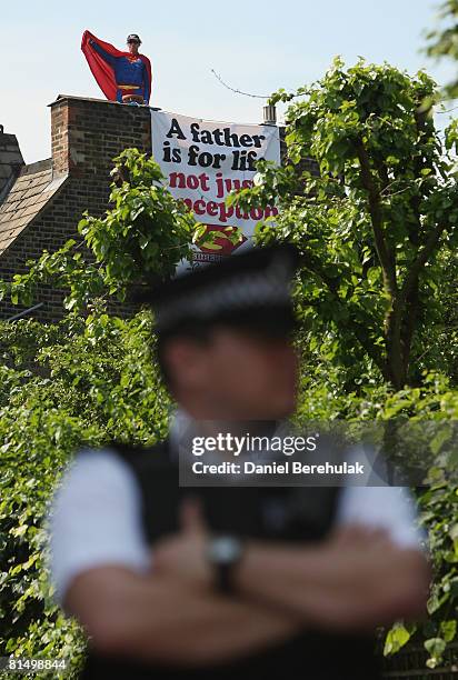 Police officer stands guard as a 'Fathers for Justice' campaigner stands atop Deputy Labour Leader Harriet Harman's home on June 9, 2008 in south...