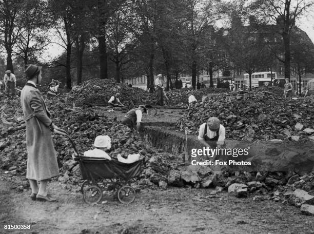 Nurse and her charge watch as workmen dig air raid shelter trenches on Streatham Common, south London, 27th September 1938.