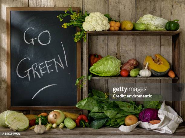 frisches marktgemüse auf alte rustikale holzregale und einem tisch und einige in eine wiederverwendbare baumwoll-einkaufstasche neben einer tafel mit "go green!" in weißer kreide vor einem alten holzbrett wand hintergrund geschrieben. - chalk bag stock-fotos und bilder