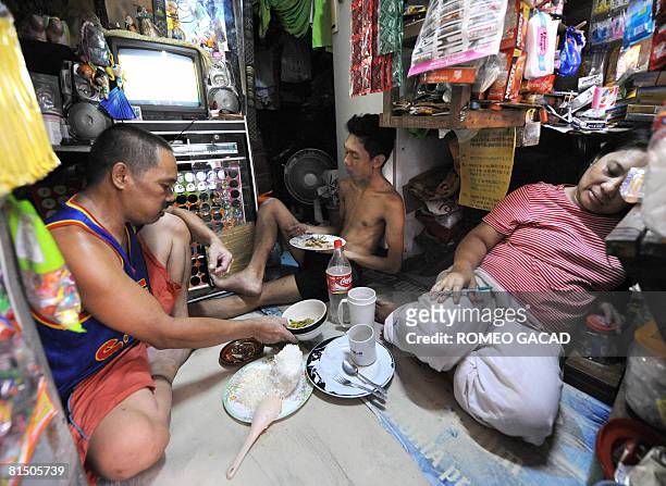Manila squatter resident Judy Asilo and wife Josephine and one of their two children eat a meal of rice and vegetable in their small room cramped...