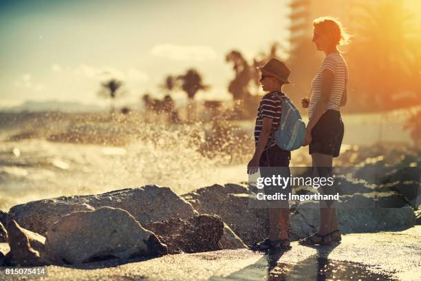 mother and son enjoying waves crashing on rocks - malaga beach stock pictures, royalty-free photos & images