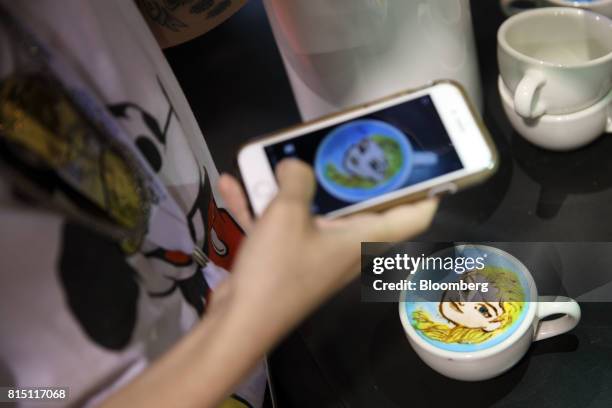 An attendee uses a mobile device to take a photograph of a coffee drink with a painted face of Elsa from "Frozen" during the D23 Expo 2017 in...