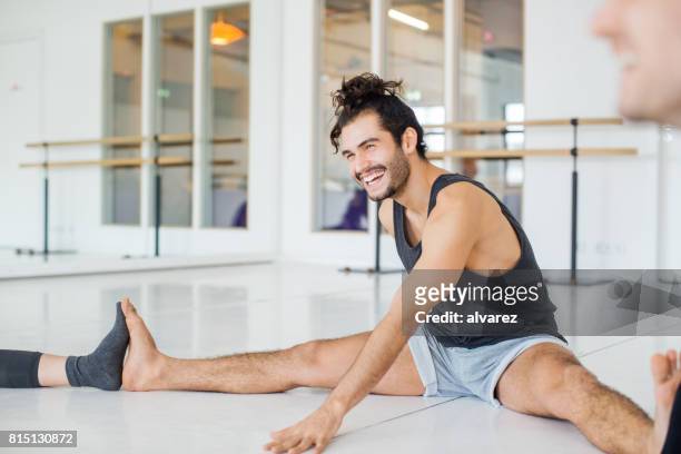 glimlachende man doen die zich uitstrekt in ballet studio - balletdanser stockfoto's en -beelden