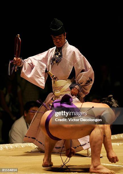 High-ranking referee or "tate-gyoji", recognized by his purple and white tassled fan, watches as Sumo wrestler Ama gets set in his position during...