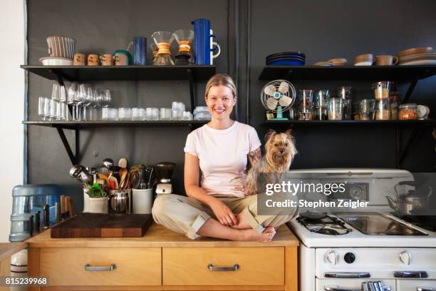 young woman sitting in her kitchen with her dog - 犬　正面 ストックフォトと画像