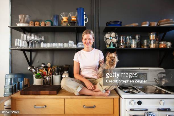 young woman sitting in her kitchen with her dog - small room stock pictures, royalty-free photos & images